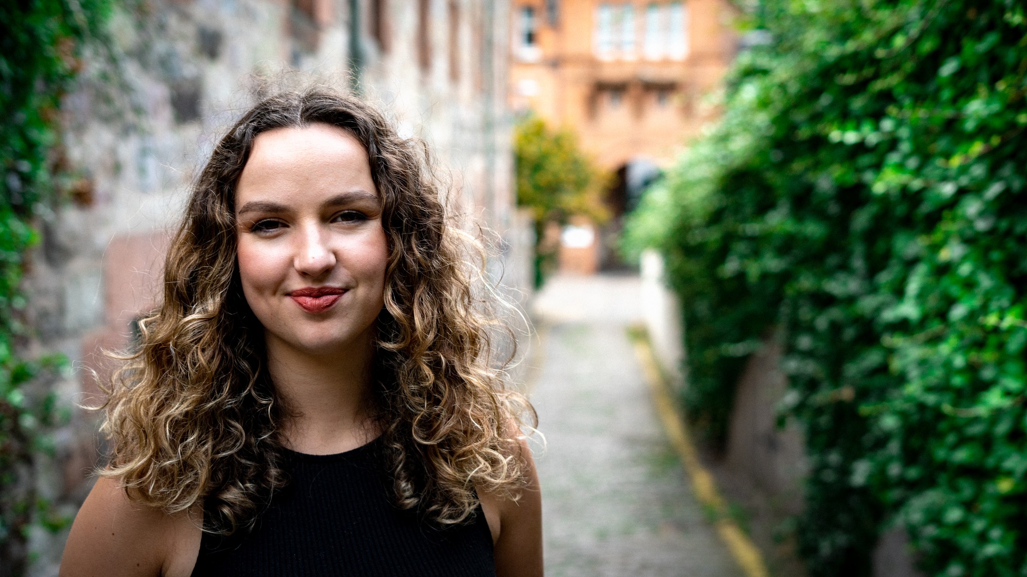 Singer Claire Frances MacNeil stands smiling in a lane surrounding by green foliage.